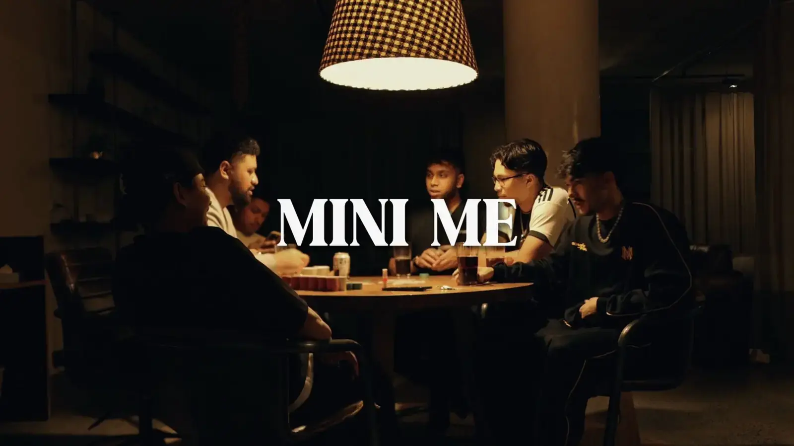 Film still of four people around a dinner table under a pendant light.
